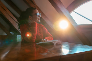 Woman looking at beautiful view in big window and smiling after reading a book at attic mansard...