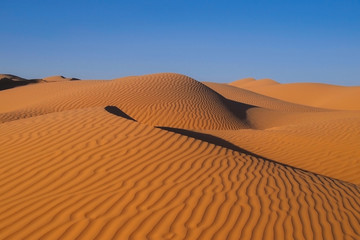 the sahara desert with red sand and beautiful wave pattern and blue sky