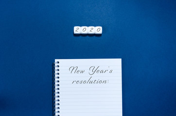 2020 written on white cubes  withe notepad in a conceptual image of the coming new year and new year resolutions,  Over blue background.