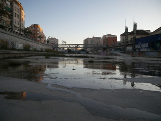 Fototapeta na wymiar Dry riverbed of the Guadalmedina river in Málaga, Spain, with just a few small streams or puddles of water on the concrete ground and grass