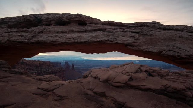 Timelapse of Mesa Arch as the sun starts to rise lighting up the clouds as the sky changes color at dawn.