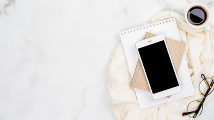 Feminine home office desk concept. White marble background with smartphone, paper notepad, glasses,...