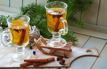 Mulled wine with Christmas spices and orange slices, anise and cinnamon sticks. Glass pubs with yellow drink on blue planks table and green spruce branch