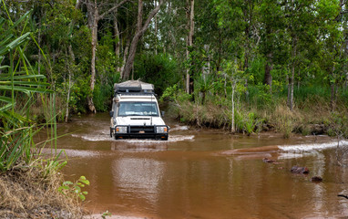 Obraz na płótnie Canvas Western Australia – Flooded Outback track crossing with 4WD car crossing a river with splashing muddy water at the bush