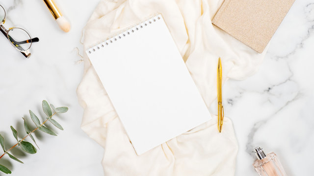 Feminine home office desk with blank paper notepad, cosmetic and fashion accessories. Flat lay, top view.