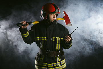 young fireman in uniform and helmet holding walkie talkie or radio set reports about emergency...