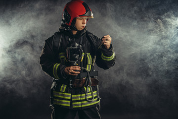 brave firefighter extinguishing fire in smoke, using special equipment and wearing uniform and helmet