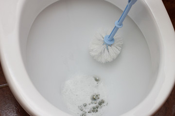 Female hands in gloves wash and disinfect a white toilet with a brush and cleaning agent