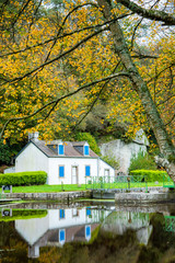 Fototapeta na wymiar Autumn on the canal from Nantes to Brest. A small white lock house is reflected in the water at the edge of a lock