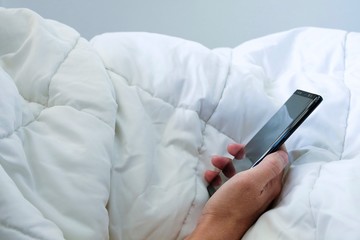 Asian men hand using smartphone texting and web browsing internet on white bed and blanket. Technology lifestyle daily routine of urban city people with copy space for text.