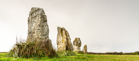 Standing stones in Brittany. Alignment of menhirs on a green meadow and under a gray sky.