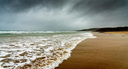 Sandy beach in winter in Brittany. The white foam of the waves of the ocean comes to die on the sand under a dark sky laden with rain.