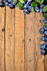 Fresh plums and leaves on rustic wooden background. Frame vIew from above and copy space.