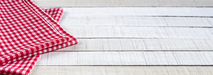 A red white checkered tea towel on white rustic wooden background. Angle view.