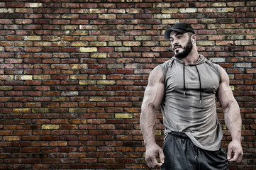 powerful strong young bearded caucasian muscle man in sport hoodie shirt wearing cap and wireless...