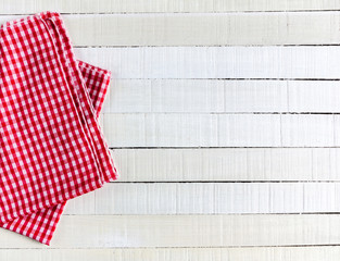 A red white checkered tea towel on white rustic wooden background. Top view.