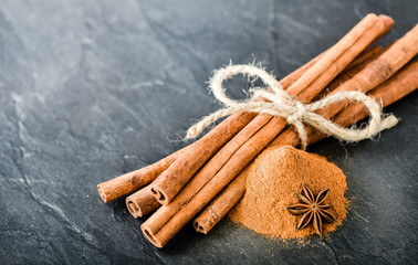 Cinnamons sticks on dark stone table. Dried cinnamon powder with star anise on black board.