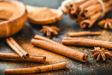 Cinnamon concept on stone table. Cinnamons sticks, powder and spices anise star on dark black board.