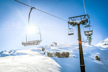 Ski lift seats high in the mountains. Winter elevator mountains panorama with sun and blue sky in...
