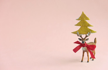 Christmas card in minimal style. Toy deer with red gift ribbon and fir tree made from dried peel on peach pink background. Happy new year concept. Copy space.