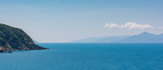 Fototapeta premium Türkisblaues Meer mit Isola d'Elba im Hintergrund und Festlandküste, Himmel und Wolken