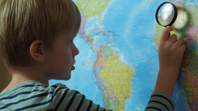 The boy looks at the map through a magnifying glass