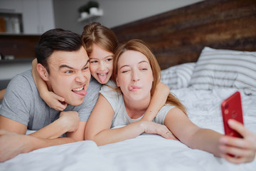 Obraz na płótnie Canvas happy caucasian parents lying on bed together with kid girl, having leisure time together at home