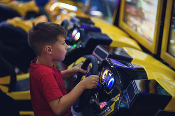 Cute European boy in red t-shirt playing car racing on slot-machine. He enjoying his spare time - 308289232