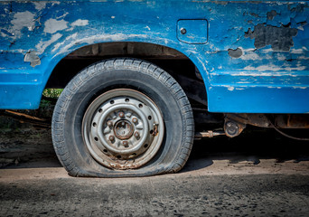 Old car cracked tires on the road, waiting for the repairman in the bright sunlight.