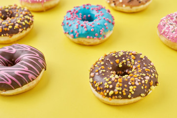 different types of colorful donats decorated sprinkles and icing on a yellow background, top view flat lay