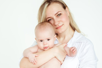 Cute infant baby on mothers hands standing in the room. Mother hugging baby with love. Happy motherhood and maternity concept