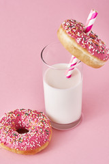 Donuts decorated with icing and sprinkle and glass of milk on a pink background