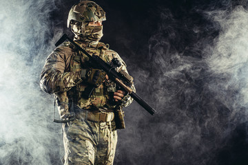 portrait of young army soldier in action with gun, dark and foggy background