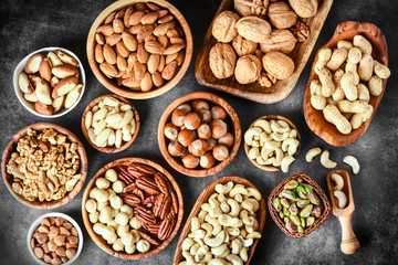 Mix of nuts in wooden bowls on dark stone table top view. Walnuts, cashew, almond, pistachio, pecan, hazelnut, macadamia nut. Healthy various super food selection.