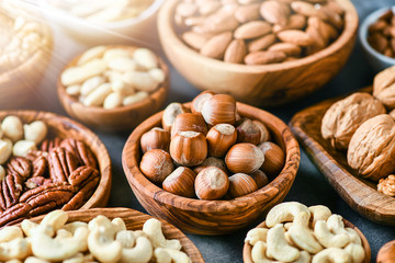 Mix of nuts in wooden bowls on dark stone table top panoramic view. Walnuts, cashew, almond, pistachio, pecan, hazelnut, macadamia nut. Healthy various super food selection with back light.