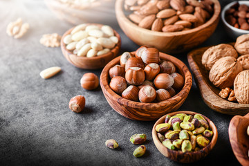 A variety of nuts in wooden bowls from top view. Walnuts, cashew, almond, pistachio, pecan, hazelnut, macadamia and peanut mix selection. Healthy fitness super food.