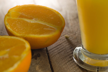 Glass of fresh orange juice with cut oranges on wooden background