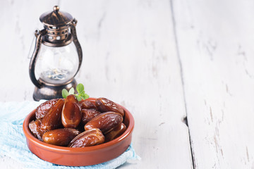 Ramadan lamp and dates still life. Raw sweet dry dates with in a terracotta bowl on a white background. Organic sweeties to healty eating