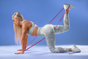 Fitness woman doing exercise for glutes isolated on blue background. Athletic girl workout with resistance band