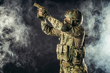 portrait of young army soldier in action with gun, dark and foggy background