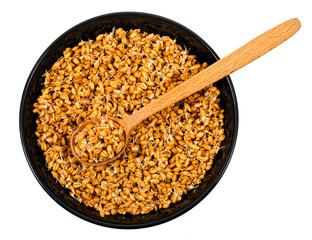 Sprouted wheat in black ceramic bowl with wooden spoon isolated on a white background. Top view.
