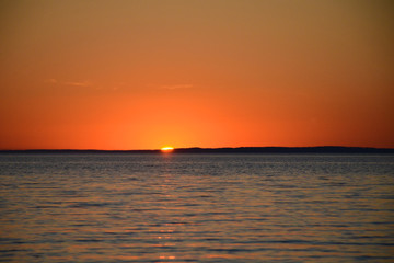 Bright sunset over the lake. Red-orange sunset. Dark water. The sun sets over the horizon.