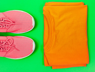 Pink sport shoes and orange t-shirt on a green background. Concept healthy lifestyle, sport and style. 