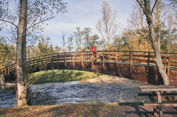 Young man and his dog watching the river from a wooden bridge on a cold autumn morning