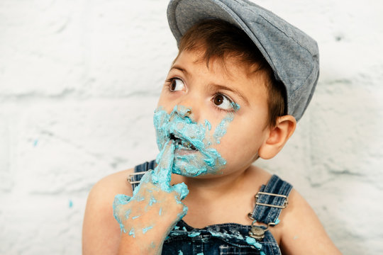 sesi&oacute;n smashcake, primer pastel de un ni&ntilde;o de 3 a&ntilde;os con pluri discapacidad. disfrutando muchismo mientras come y se ensucia de nata azul con el dedo en la boca y boina.