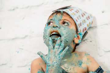 sesión smashcake, primer pastel de un niño de 3 años con pluri discapacidad. disfrutando muchismo mientras come y se ensucia de nata azul con la mano en la boca y relamiendo los dedos con la lengua