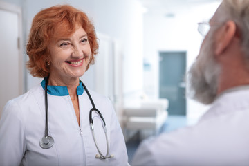 Cheerful senior female doctor talking to her colleague in hospital hall