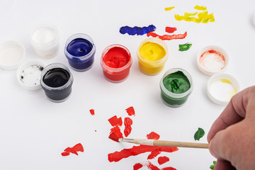 Open jars of gouache paint on a white background. The artist tries the color of paint on paper.