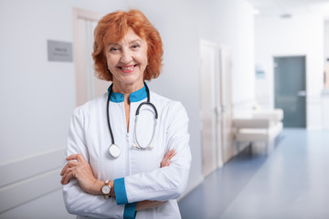 Cheerful elderly female doctor smiling to the camera. Friendly female practitioner posing confidently at her clinic