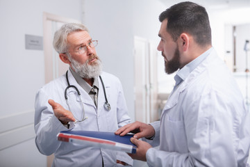 Senior doctor talking to his younger intern. Two male doctors chatting in the hall of a hospital